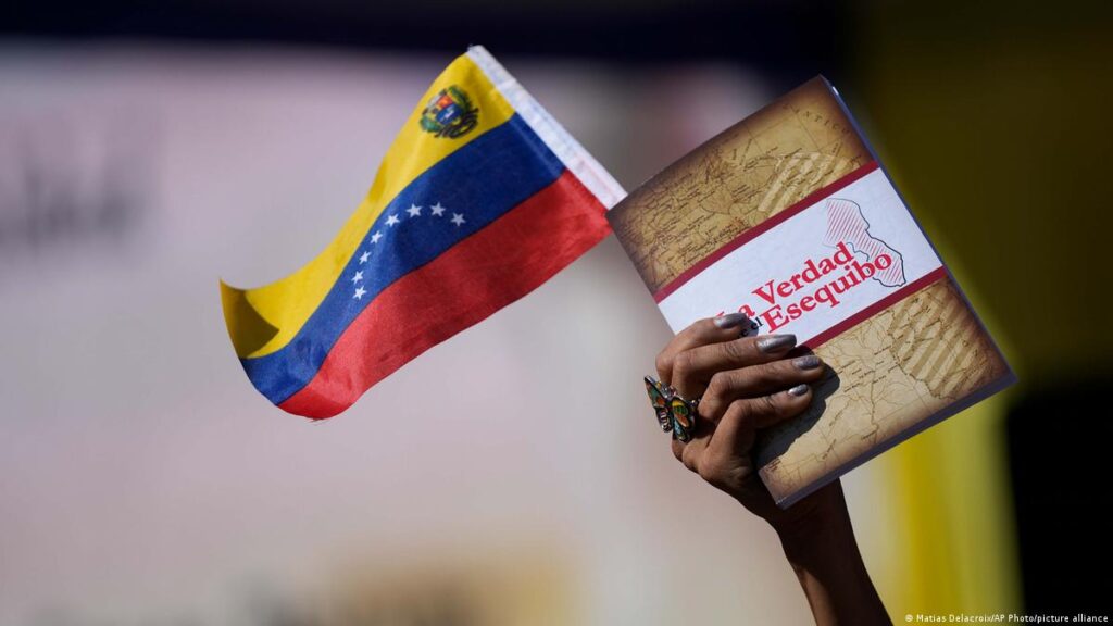 Hand of a person holding a small Venezuelan flag and a book entitled The Truth of the Essquibo. Photo: Matias Delacroix/AP.