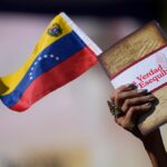 Hand of a person holding a small Venezuelan flag and a book entitled The Truth of the Essquibo. Photo: Matias Delacroix/AP.