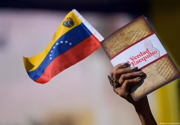 Hand of a person holding a small Venezuelan flag and a book entitled The Truth of the Essquibo. Photo: Matias Delacroix/AP.