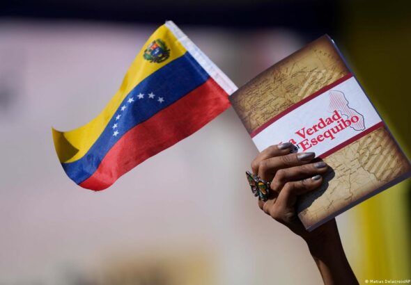 Hand of a person holding a small Venezuelan flag and a book entitled The Truth of the Essquibo. Photo: Matias Delacroix/AP.