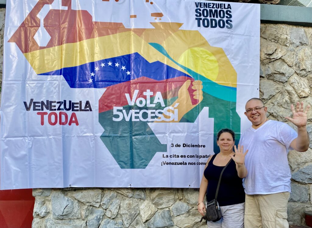 Orinoco Tribune editor, Jesus Rodriguez-Espinoza, and his wife Yullma Hernandez next to a banner for the Essequibo Referendum campaign showing the map of Venezuela (including the Essequibo territory) and the following caption: "Venezuela is all of us, all Venezuela vote 5 times yes. On December 3, we have an appointment with the homeland, Venezuela is calling us!" Photo: Orinoco Tribune.