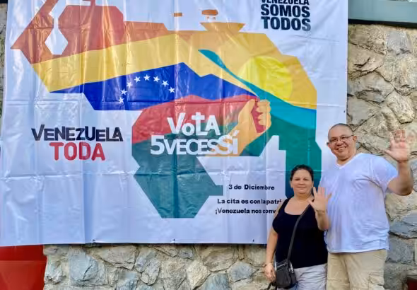 Orinoco Tribune editor, Jesus Rodriguez-Espinoza, and his wife Yullma Hernandez next to a banner for the Essequibo Referendum campaign showing the map of Venezuela (including the Essequibo territory) and the following caption: "Venezuela is all of us, all Venezuela vote 5 times yes. On December 3, we have an appointment with the homeland, Venezuela is calling us!" Photo: Orinoco Tribune.