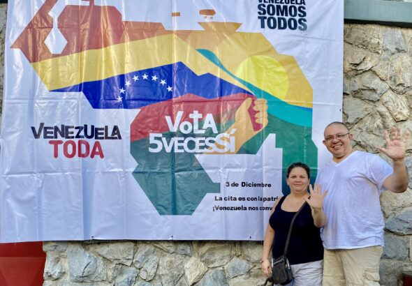 Orinoco Tribune editor, Jesus Rodriguez-Espinoza, and his wife Yullma Hernandez next to a banner for the Essequibo Referendum campaign showing the map of Venezuela (including the Essequibo territory) and the following caption: "Venezuela is all of us, all Venezuela vote 5 times yes. On December 3, we have an appointment with the homeland, Venezuela is calling us!" Photo: Orinoco Tribune.