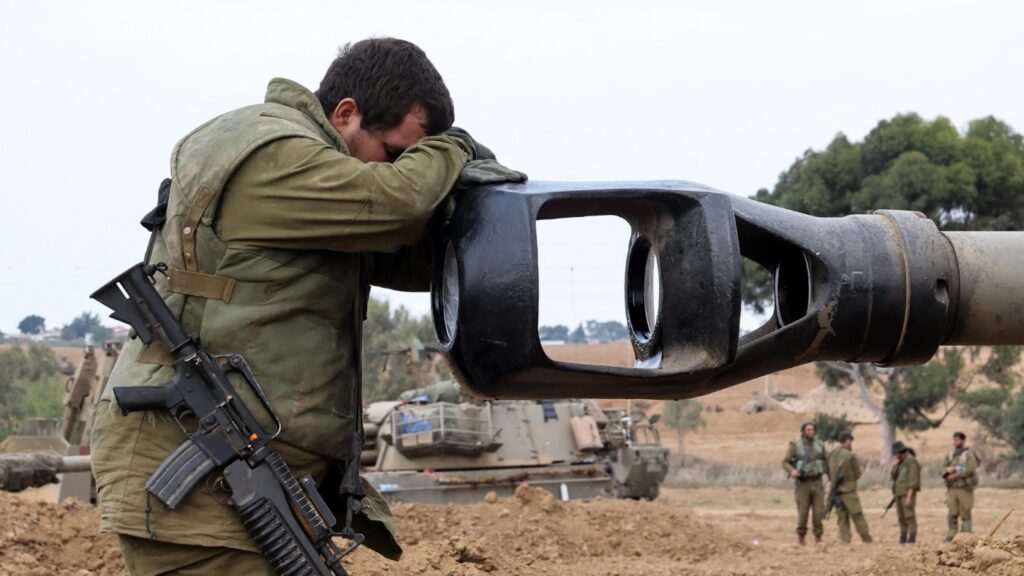 An Israeli Occupation Forces soldier rests his head on an artillery gun barrel of an armored vehicle as troops take position near the Gaza wall on October 9,  2023. Photo: AFP.