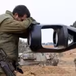 An Israeli Occupation Forces soldier rests his head on an artillery gun barrel of an armored vehicle as troops take position near the Gaza wall on October 9,  2023. Photo: AFP.