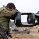 An Israeli Occupation Forces soldier rests his head on an artillery gun barrel of an armored vehicle as troops take position near the Gaza wall on October 9,  2023. Photo: AFP.