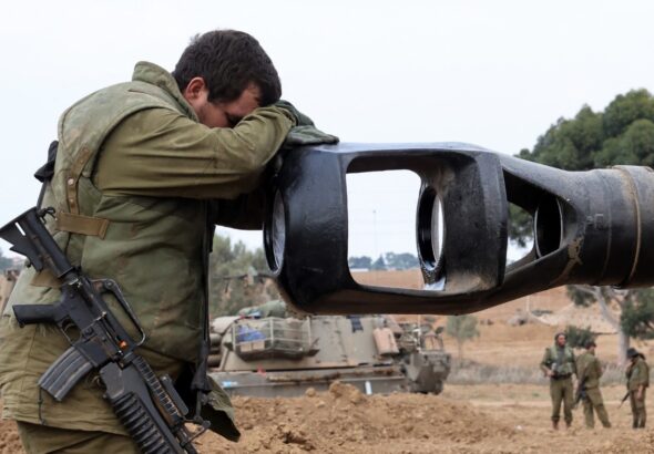 An Israeli Occupation Forces soldier rests his head on an artillery gun barrel of an armored vehicle as troops take position near the Gaza wall on October 9,  2023. Photo: AFP.
