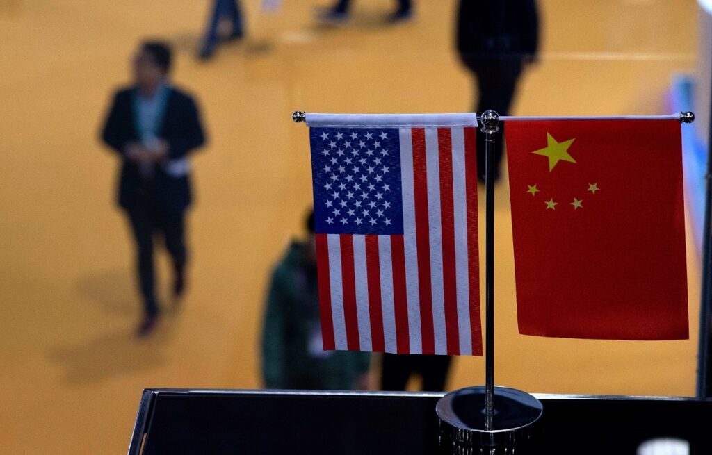 Small stand flags of the US and China on an elevated desk with blurred people passing by below it. Photo: J. Eisele/Getty Images/AFP.