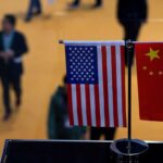 Small stand flags of the US and China on an elevated desk with blurred people passing by below it. Photo: J. Eisele/Getty Images/AFP.