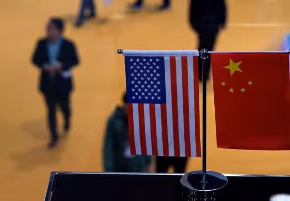 Small stand flags of the US and China on an elevated desk with blurred people passing by below it. Photo: J. Eisele/Getty Images/AFP.