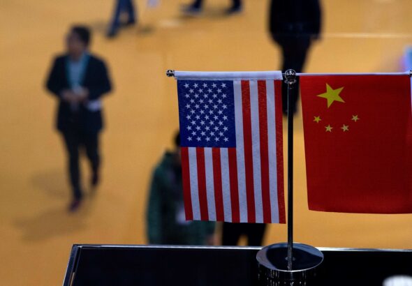 Small stand flags of the US and China on an elevated desk with blurred people passing by below it. Photo: J. Eisele/Getty Images/AFP.