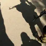 The image shows the shadows of two people, one person with a camera and the other with a gun. Photo: Kirill Kudryavtsev/AFP 2023.