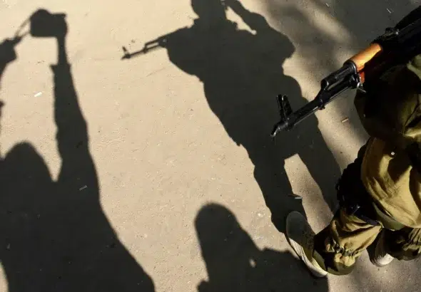 The image shows the shadows of two people, one person with a camera and the other with a gun. Photo: Kirill Kudryavtsev/AFP 2023.