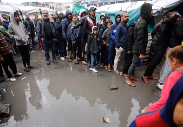 Palestinian refugees in line for food in the rain outside the shelter in Deir al-Balah. Photo: UNRWA.