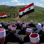Druze men sit with Syrian flags during a rally marking Syria's Independence Day, in the Druze village of Majdal Shams in the Israeli-occupied Golan Heights, on the border with Syria, Monday, April 17, 2023. Photo: AP.