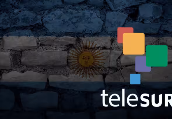 Photo composition showing the logo of Telesur over a transparent flag of Argentina on a wall of stone. Photo: Telesur/File photo.