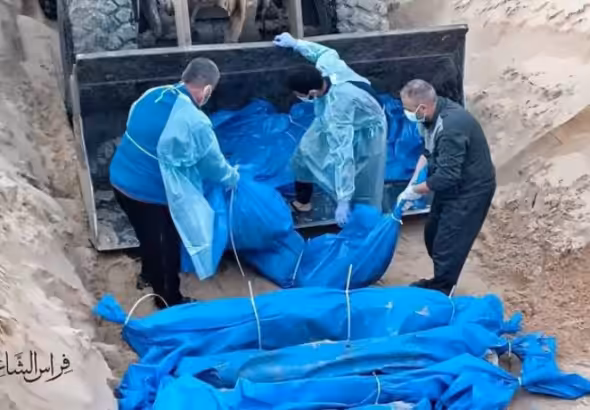 The photo shows people lowering the bodies of deceased Palestinians into a mass grave, wrapped in blue bags. Photo: Eye on Palestine.