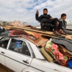 Two Palestinian children ride atop a vehicle in Rafah, February 13, 2024. Photo: Mohammed Abed/AFP.