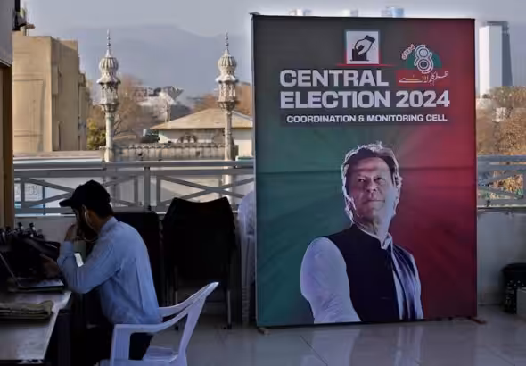 A supporter of Pakistan's imprisoned former Prime Minister, Imran Khan, works on a desk next to a poster of the leader displayed at his party office, in Islamabad, Pakistan, February 9, 2024. Photo: AP.