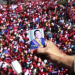 A person holds a photo of Hugo Chavez over a bridge overlooking a crowd of Chavistas who went to the streets of Caracas to bid a final goodbye to President Hugo Chávez on March 6, 2013. Photo: Ricardo Mazalan/AP.