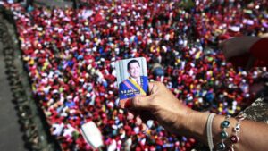 A person holds a photo of Hugo Chavez over a bridge overlooking a crowd of Chavistas who went to the streets of Caracas to bid a final goodbye to President Hugo Chávez on March 6, 2013. Photo: Ricardo Mazalan/AP.