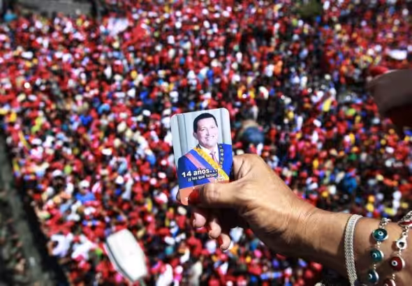 A person holds a photo of Hugo Chavez over a bridge overlooking a crowd of Chavistas who went to the streets of Caracas to bid a final goodbye to President Hugo Chávez on March 6, 2013. Photo: Ricardo Mazalan/AP.
