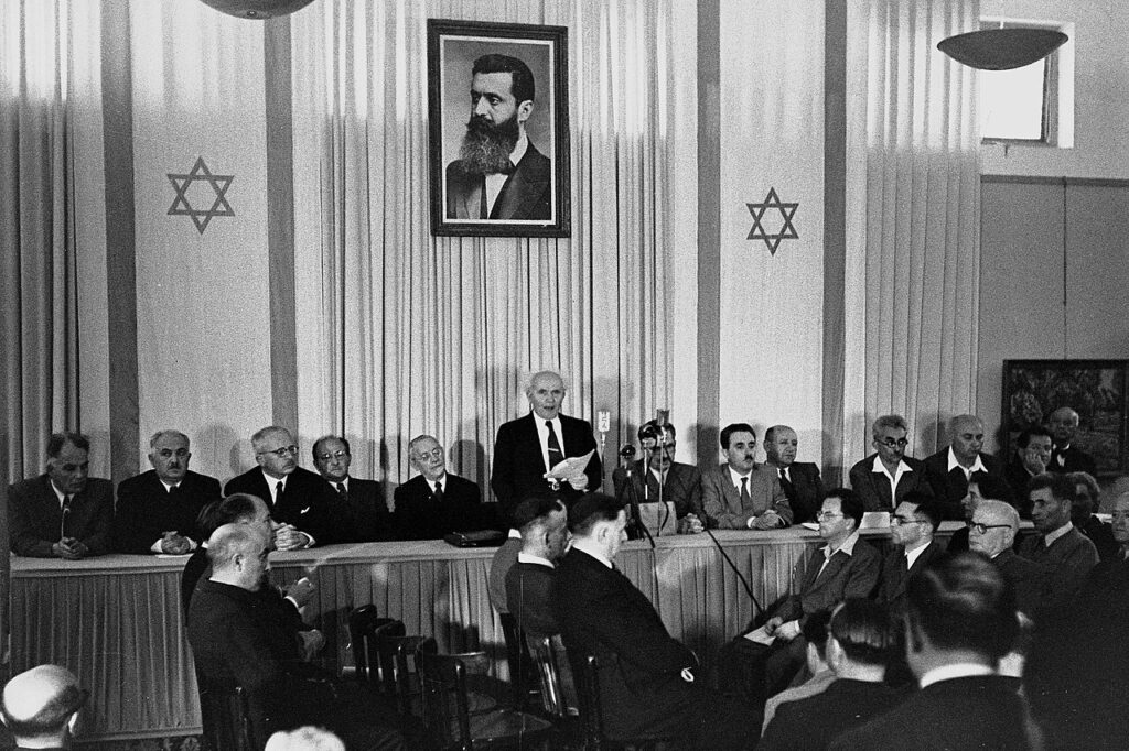 Ben Gurion proclaims the “State of Israel” in a museum in Tel Aviv, under the portrait of Theodor Herzl, founder of the zionist movement, on May 14, 1948. Photo: Wikimedia Commons / Rudi Weissenstein.