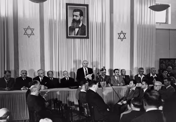 Ben Gurion proclaims the “State of Israel” in a museum in Tel Aviv, under the portrait of Theodor Herzl, founder of the zionist movement, on May 14, 1948. Photo: Wikimedia Commons / Rudi Weissenstein.