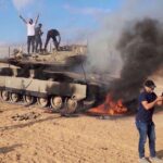 Palestinians celebrate next to a destroyed Israeli tank at the Gaza Strip fence on October 7, 2023. Photo: AP.