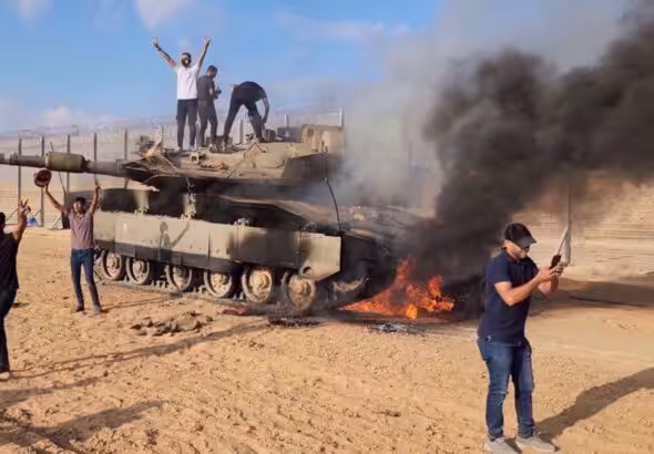 Palestinians celebrate next to a destroyed Israeli tank at the Gaza Strip fence on October 7, 2023. Photo: AP.