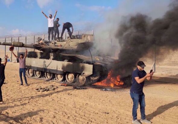 Palestinians celebrate next to a destroyed Israeli tank at the Gaza Strip fence on October 7, 2023. Photo: AP.