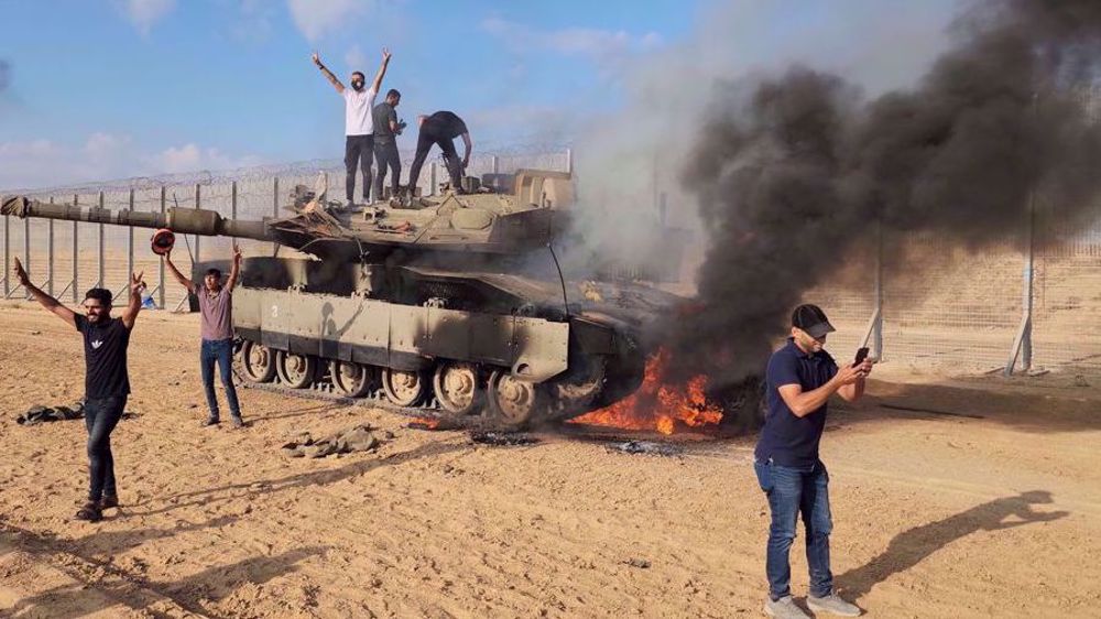 Palestinians celebrate next to a destroyed Israeli tank at the Gaza Strip fence on October 7, 2023. Photo: AP.