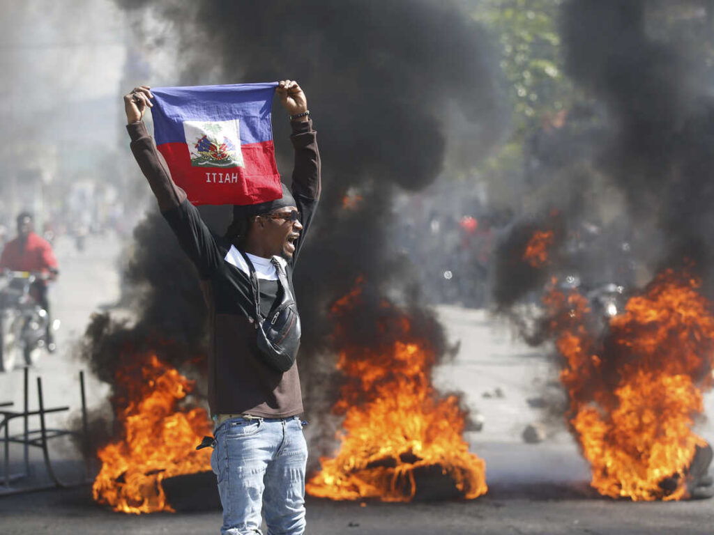 A demonstrator holds up a Haitian flag during protests demanding the resignation of de facto prime minister Ariel Henry in Port-au-Prince, Haiti, on Friday, March 1, 2024. Photo: Odelyn Joseph/AP.