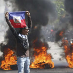 A demonstrator holds up a Haitian flag during protests demanding the resignation of de facto prime minister Ariel Henry in Port-au-Prince, Haiti, on Friday, March 1, 2024. Photo: Odelyn Joseph/AP.