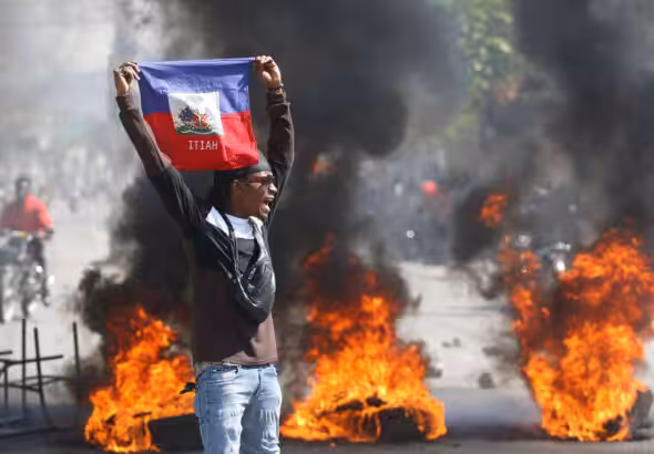 A demonstrator holds up a Haitian flag during protests demanding the resignation of de facto prime minister Ariel Henry in Port-au-Prince, Haiti, on Friday, March 1, 2024. Photo: Odelyn Joseph/AP.