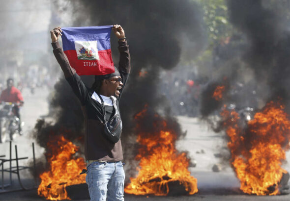 A demonstrator holds up a Haitian flag during protests demanding the resignation of de facto prime minister Ariel Henry in Port-au-Prince, Haiti, on Friday, March 1, 2024. Photo: Odelyn Joseph/AP.