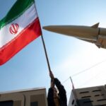 A person holding an Iranian flag next to a missile. Photo: File photo.
