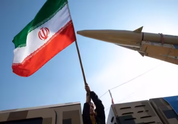 A person holding an Iranian flag next to a missile. Photo: File photo.