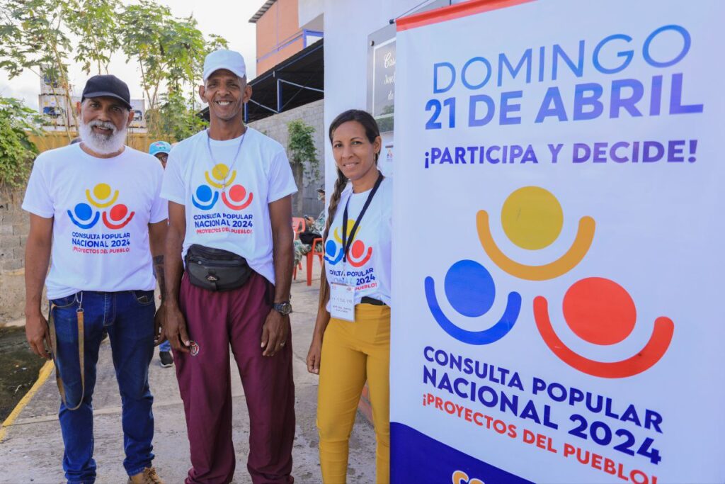 People wearing "2024 National Popular Consultation" t-shirts next to a banner with the logo of the electoral consultation. Photo: Venezuelan Ministry of Science and Technology.