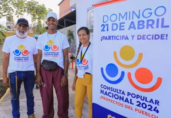People wearing "2024 National Popular Consultation" t-shirts next to a banner with the logo of the electoral consultation. Photo: Venezuelan Ministry of Science and Technology.