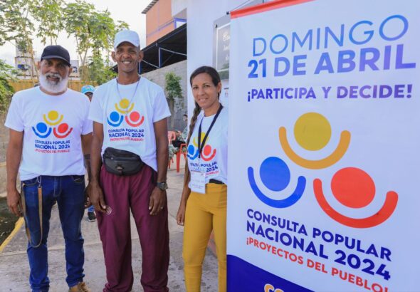 People wearing "2024 National Popular Consultation" t-shirts next to a banner with the logo of the electoral consultation. Photo: Venezuelan Ministry of Science and Technology.
