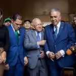 Luis Eduardo Martinez (center-right) buttoning up his suit while Democratic Action's Bernabe Gutierrez (center) talks to him, before issuing statements to the press on Monday, April 22, 2024. Photo: QuePasaMedia.