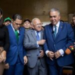 Luis Eduardo Martinez (center-right) buttoning up his suit while Democratic Action's Bernabe Gutierrez (center) talks to him, before issuing statements to the press on Monday, April 22, 2024. Photo: QuePasaMedia.