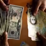 People holding US dollar banknotes and Venezuelan bolívar banknotes. Photo: Juan Barreto/AFP/Getty Images/File photo.