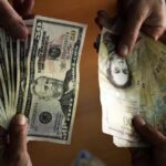 People holding US dollar banknotes and Venezuelan bolívar banknotes. Photo: Juan Barreto/AFP/Getty Images/File photo.