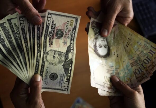 People holding US dollar banknotes and Venezuelan bolívar banknotes. Photo: Juan Barreto/AFP/Getty Images/File photo.