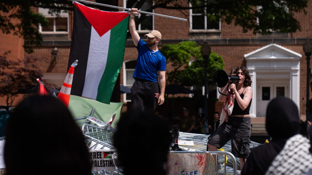 People stand atop a pile of barricades as they lead a chant at an encampment by students protesting against Israel at George Washington University, April 30, 2024. Mark Schiefelbein. Photo: AP.