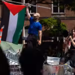 People stand atop a pile of barricades as they lead a chant at an encampment by students protesting against Israel at George Washington University, April 30, 2024. Mark Schiefelbein. Photo: AP.