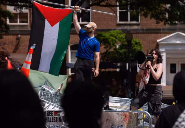 People stand atop a pile of barricades as they lead a chant at an encampment by students protesting against Israel at George Washington University, April 30, 2024. Mark Schiefelbein. Photo: AP.