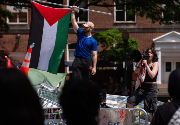 People stand atop a pile of barricades as they lead a chant at an encampment by students protesting against Israel at George Washington University, April 30, 2024. Mark Schiefelbein. Photo: AP.